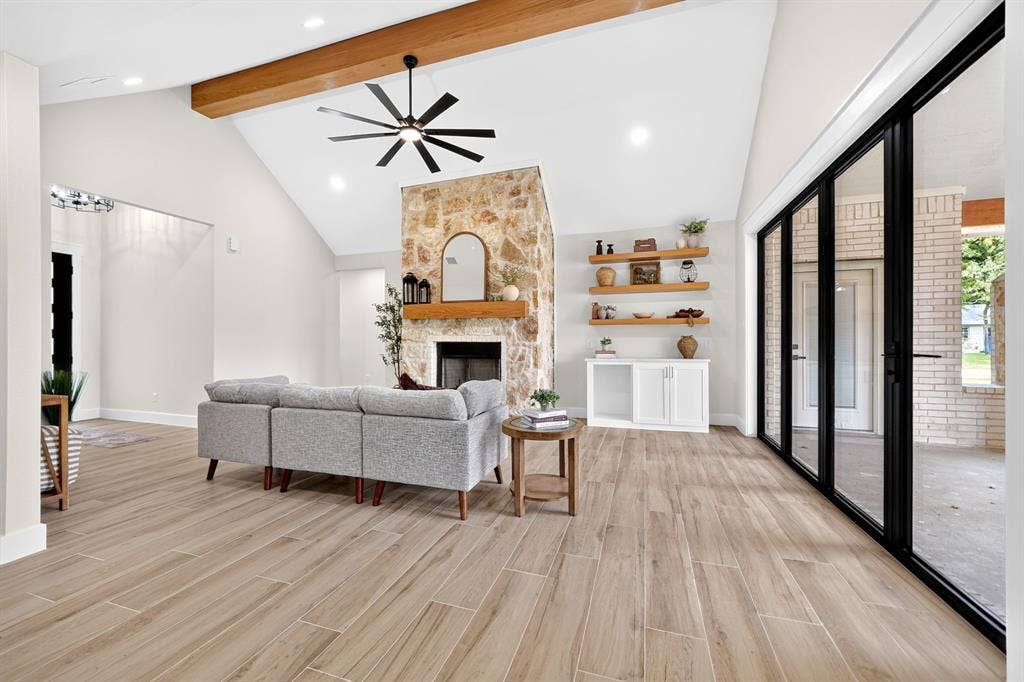 120 Springwood Road, Enchanted Oaks, TX 75156 Vaulted ceiling with exposed wood beam, natural stone fireplace, wood-finish flooring, built-in shelving, and multi-panel sliding glass doors