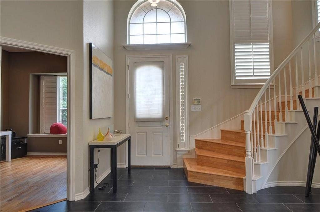 8626 Forest Glen Drive, Irving, TX 75063 Entryway featuring dark tile flooring, a curved staircase with wood-finish treads and white risers, and a prominent arched transom window above the entry door