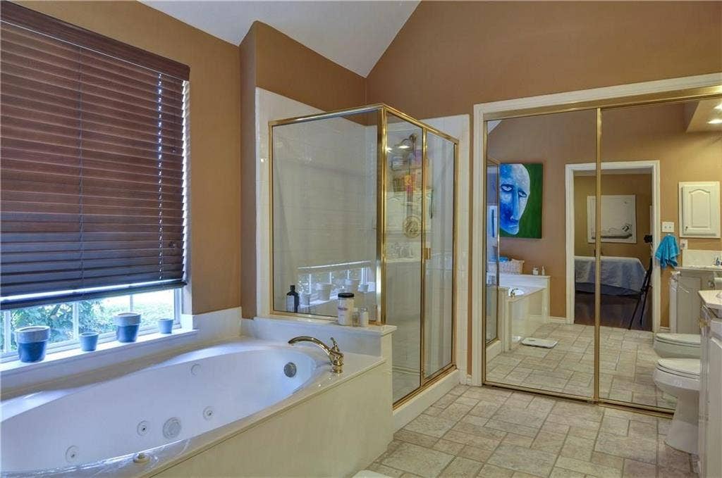 8626 Forest Glen Drive, Irving, TX 75063 Integrated soaking tub with brass-finish fixtures, glass-enclosed shower with brass-finish framing, mirrored wardrobe doors, and tiled flooring