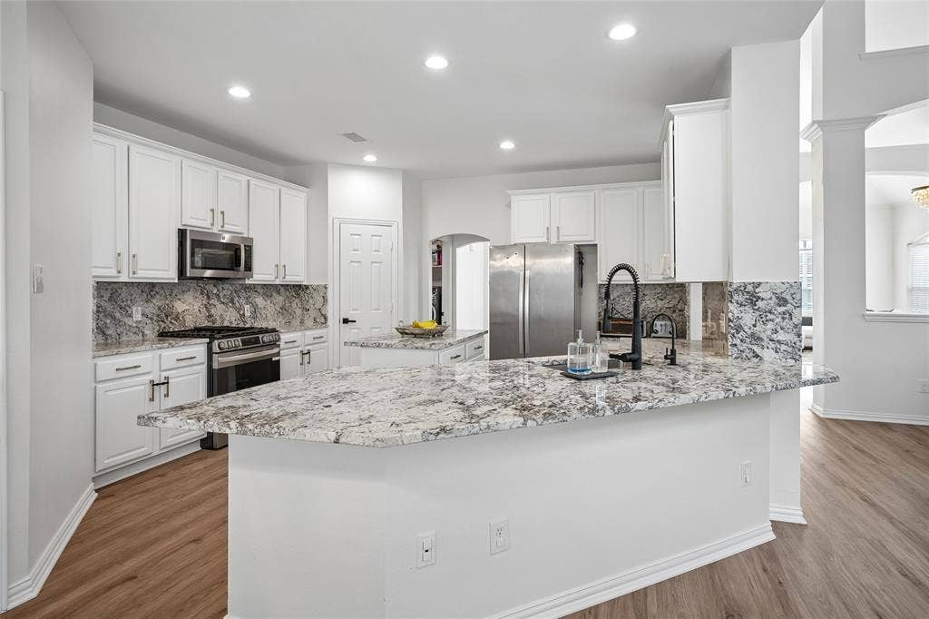 3801 Kite Meadow Drive, Plano, TX 75074 White cabinetry, stainless steel appliances, dark wood-finish flooring, recessed lighting, and a kitchen island with stone countertops