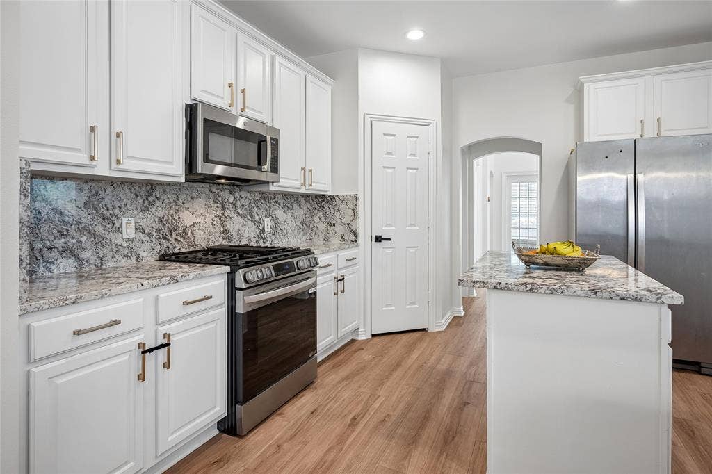 3801 Kite Meadow Drive, Plano, TX 75074 Kitchen featuring white cabinetry, granite countertops, stainless steel appliances, wood-finish flooring, and a central island