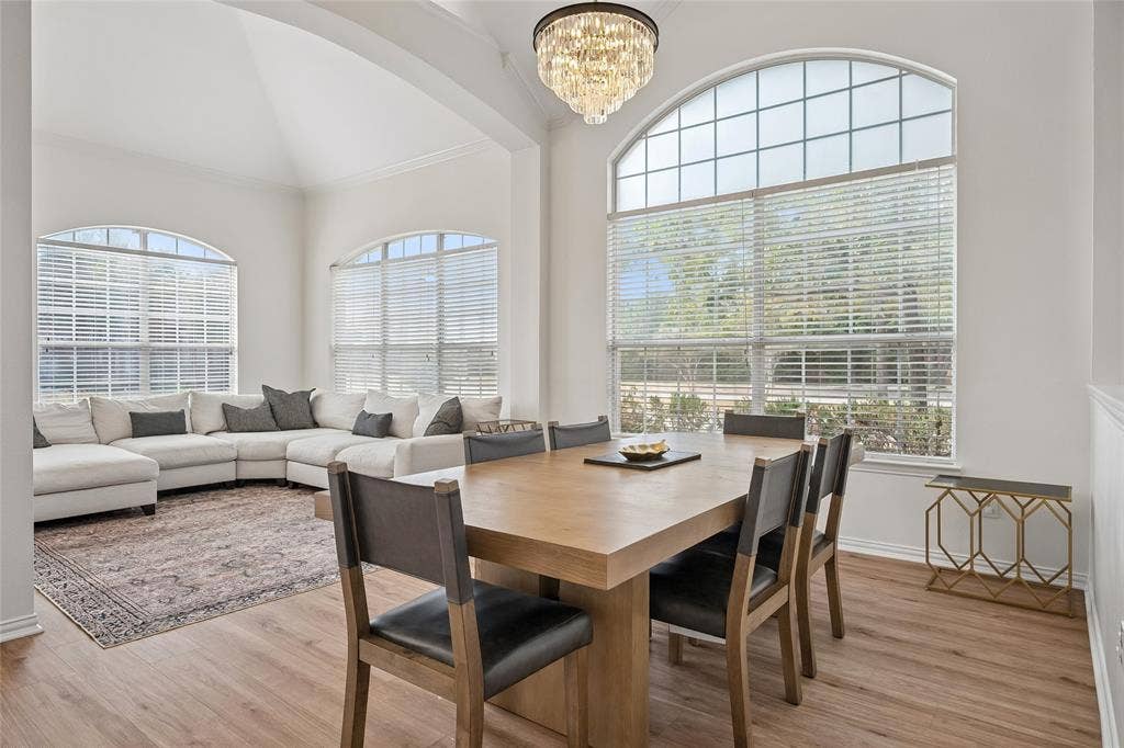3801 Kite Meadow Drive, Plano, TX 75074 Vaulted ceiling, arched windows with blinds, wood-finish flooring, and a crystal chandelier