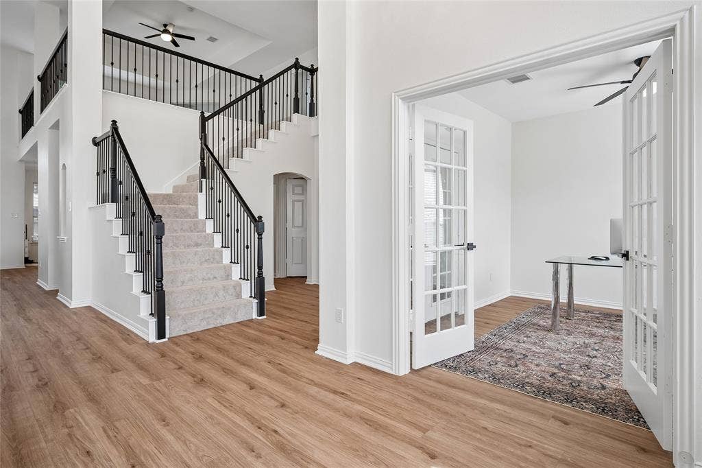 3801 Kite Meadow Drive, Plano, TX 75074 Double-height entry with wood-finish flooring, a carpeted staircase with wrought iron balusters, and a room featuring French doors