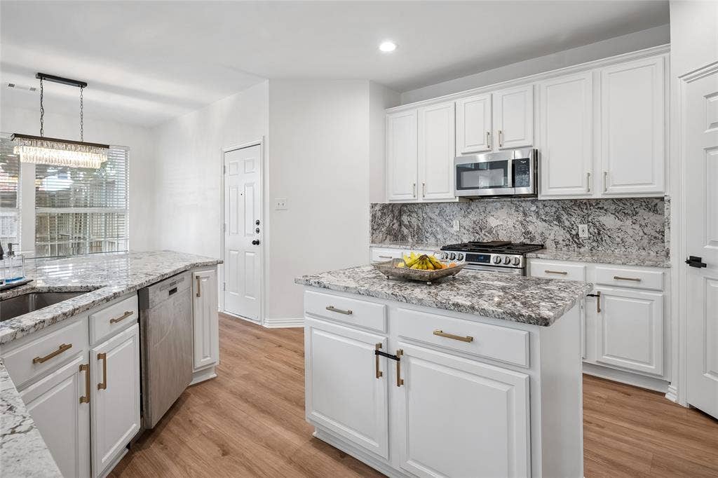 3801 Kite Meadow Drive, Plano, TX 75074 Kitchen featuring white cabinetry, granite countertops, stainless steel appliances, a central island, and wood-finish flooring