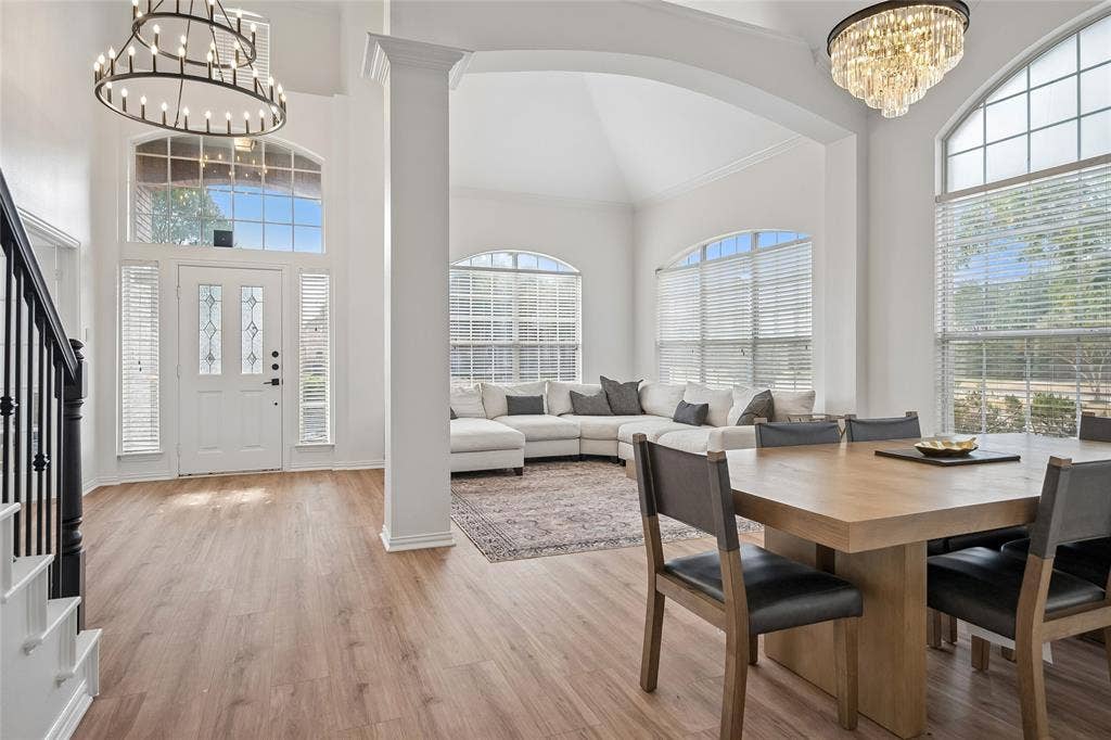 3801 Kite Meadow Drive, Plano, TX 75074 High vaulted ceilings with decorative chandeliers, wood-finish flooring, a white paneled entry door with decorative glass inserts, and multiple arched windows