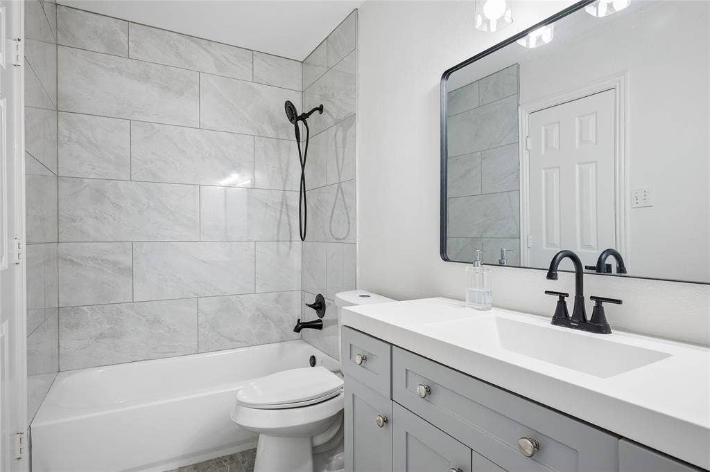 3801 Kite Meadow Drive, Plano, TX 75074 White bathtub with a tile surround, a single vanity with a white countertop, and a rectangular framed mirror