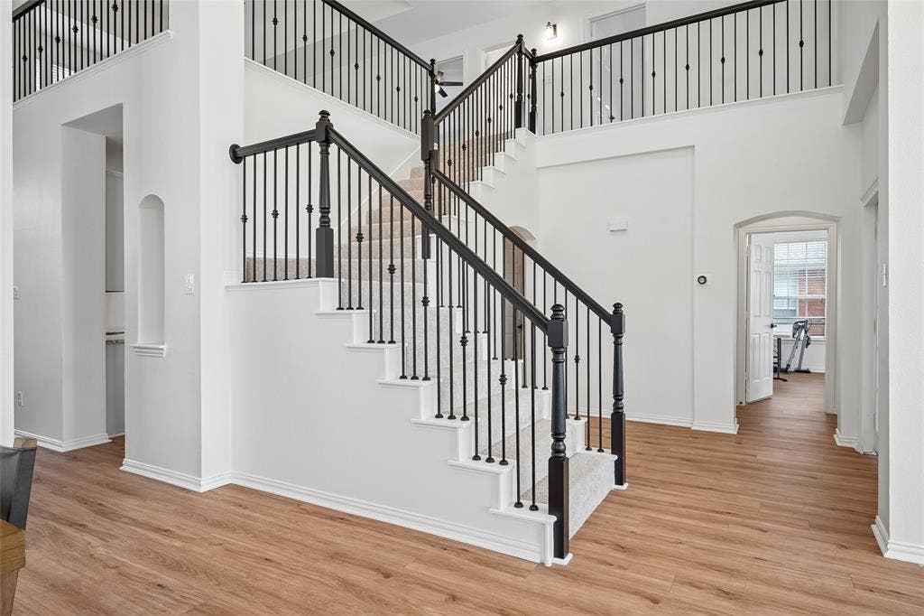 3801 Kite Meadow Drive, Plano, TX 75074 Two-story foyer with wood-finish flooring, a grand staircase featuring wrought-iron balusters and dark wood newel posts, and an arched entryway