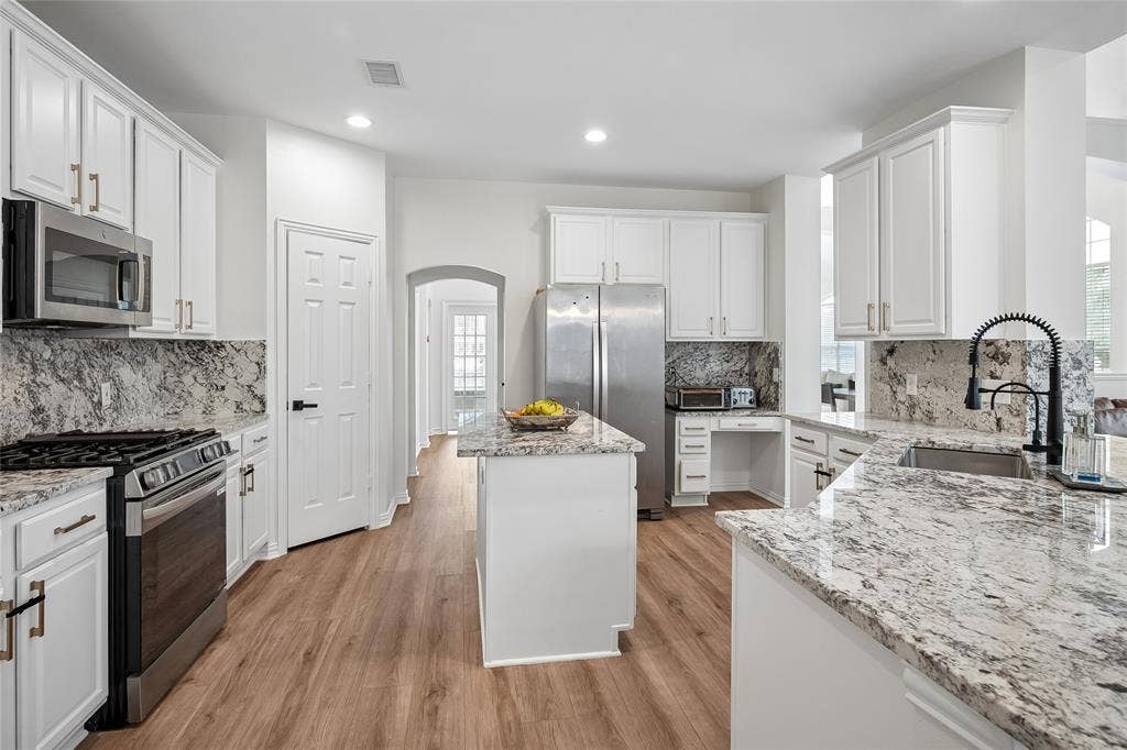 3801 Kite Meadow Drive, Plano, TX 75074 Kitchen featuring white cabinetry, light-toned wood-finish flooring, stainless steel appliances, a center island, and stone countertops