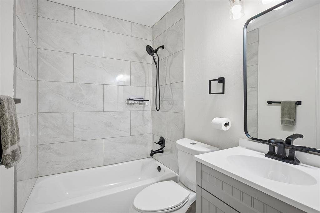 3801 Kite Meadow Drive, Plano, TX 75074 Bathroom featuring a white bathtub, large format tile shower surround, matte black fixtures, a single vanity with a white countertop, and a framed mirror