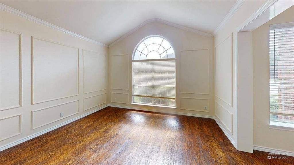 Vaulted ceiling, wood-finish flooring, decorative wall paneling, arched window, and horizontal window blinds