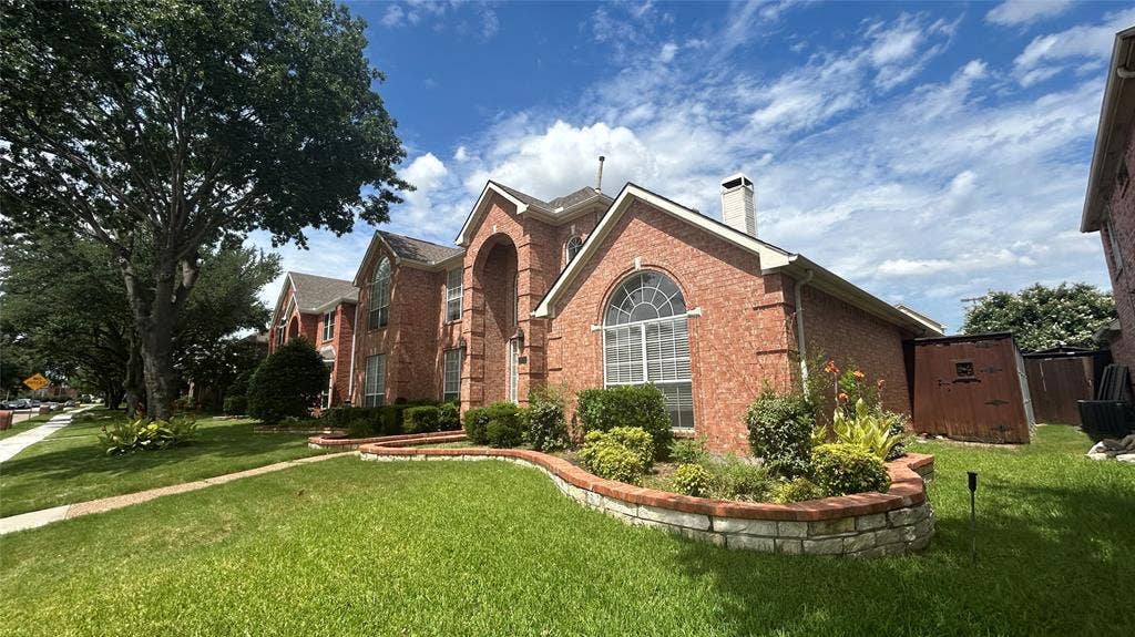 Brick exterior with arched entry, arched window, chimney, and landscaped garden beds with stone and brick retaining walls
