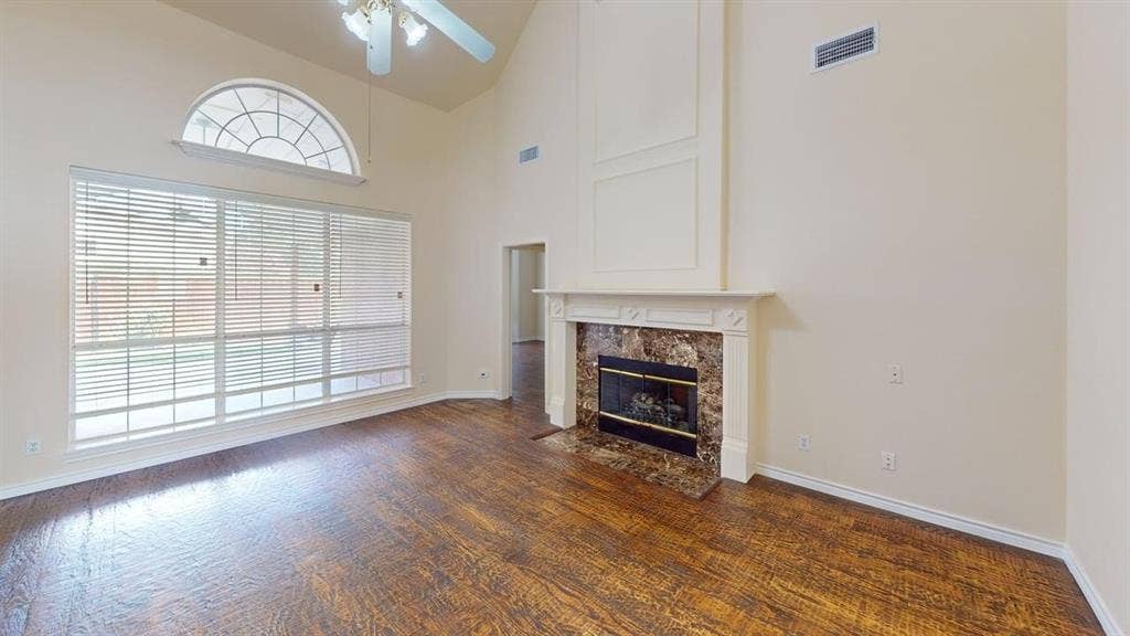 Vaulted ceiling, wood-finish flooring, large window with arch transom, fireplace with stone surround, and decorative wall paneling