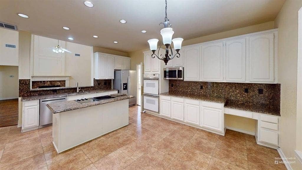 Kitchen featuring an island, integrated cooktop, double wall ovens, white cabinetry, and stone-look countertops with matching backsplash