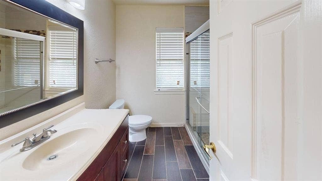 Vanity with integrated sink, framed mirror, wood-finish flooring, and glass-enclosed shower