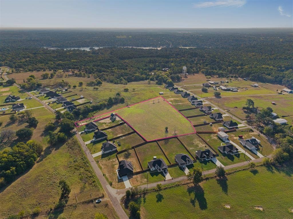 15610 County Road 436, Lindale, TX 75771 Expansive land parcel featuring clear, undeveloped terrain within a residential area, surrounded by established properties, with distant water visible