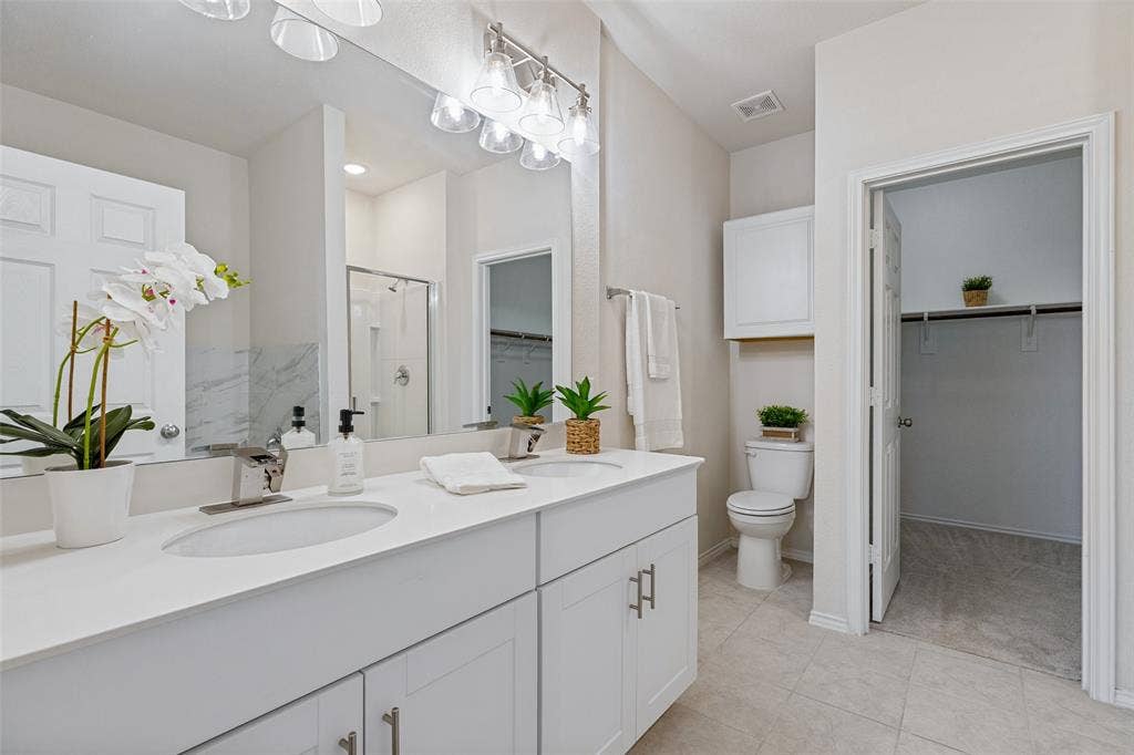 Beautiful master bathroom with dual sinks, quartz countertops, decorative lighting, extra cabinet space, along with a large walk-in closet