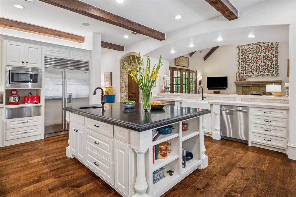 5222 Stonegate Road, Dallas, TX 75209 Open to the great room, kitchen features hardwood flooring, white cabinetry, stainless steel appliances, dark countertop on kitchen island, and a built-in kitchen island with shelving
