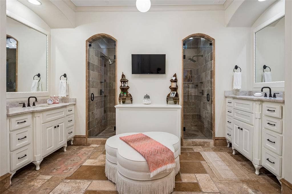 5222 Stonegate Road, Dallas, TX 75209 Primary bath offers dual vanity sinks with white cabinetry and framed mirrors, two glass-enclosed showers with tiled interiors, and stone-finish flooring