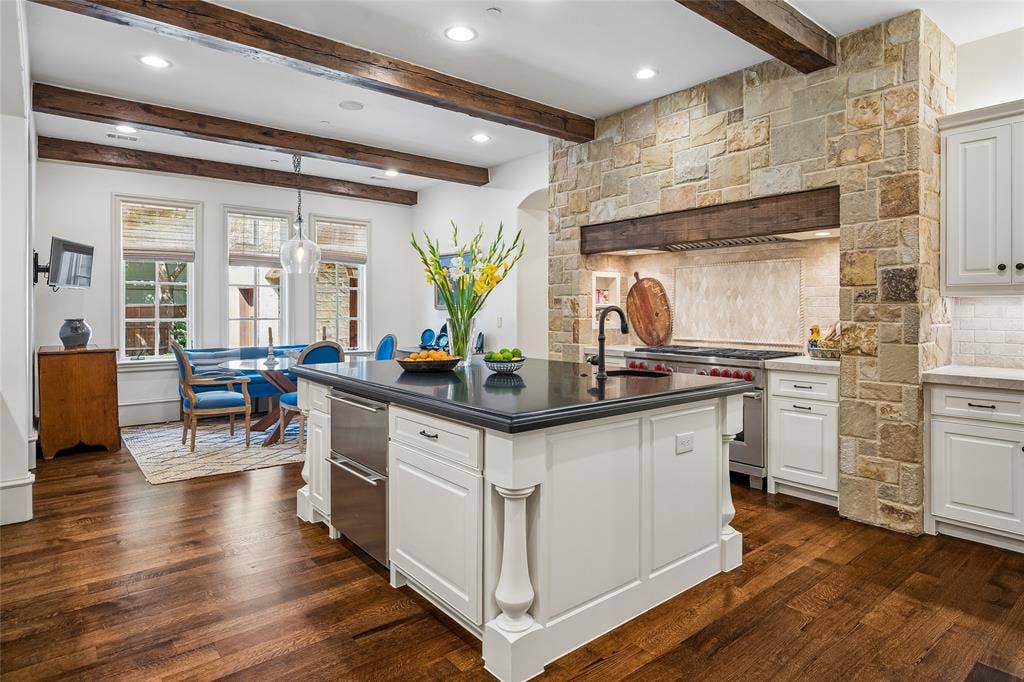 5222 Stonegate Road, Dallas, TX 75209 Gourmet kitchen featuring a stone-clad range hood, wood-beamed ceiling, wood-finish flooring, white cabinetry, and a center island with a dark countertop