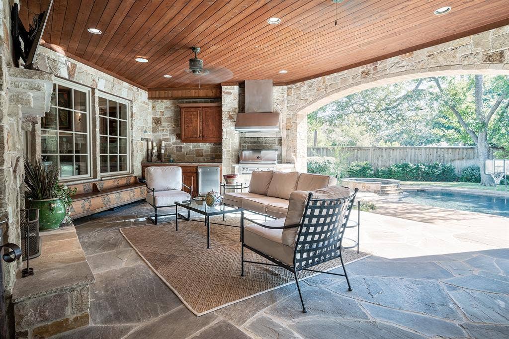 5222 Stonegate Road, Dallas, TX 75209 Covered outdoor living space featuring flagstone flooring, a natural stone fireplace, recessed lighting, and a built-in outdoor kitchen with wooden cabinetry
