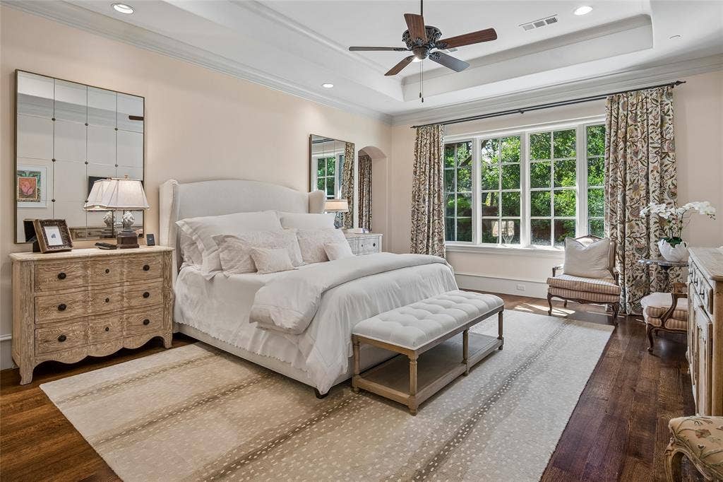5222 Stonegate Road, Dallas, TX 75209 First floor primary bedroom. Hardwood flooring, tray ceiling with recessed lighting, ceiling fan, and large windows with transom panes