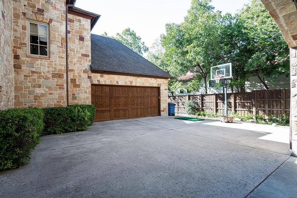 5222 Stonegate Road, Dallas, TX 75209 Stone veneer exterior, multi-car garage with wood-finish doors, expansive concrete driveway, and cedar privacy fencing