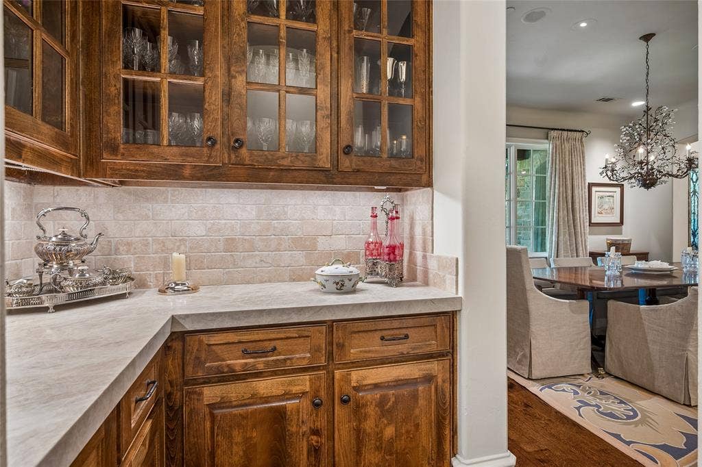 5222 Stonegate Road, Dallas, TX 75209 Rich wood-finish cabinetry with glass panel inserts, light-toned countertop, and tiled backsplash