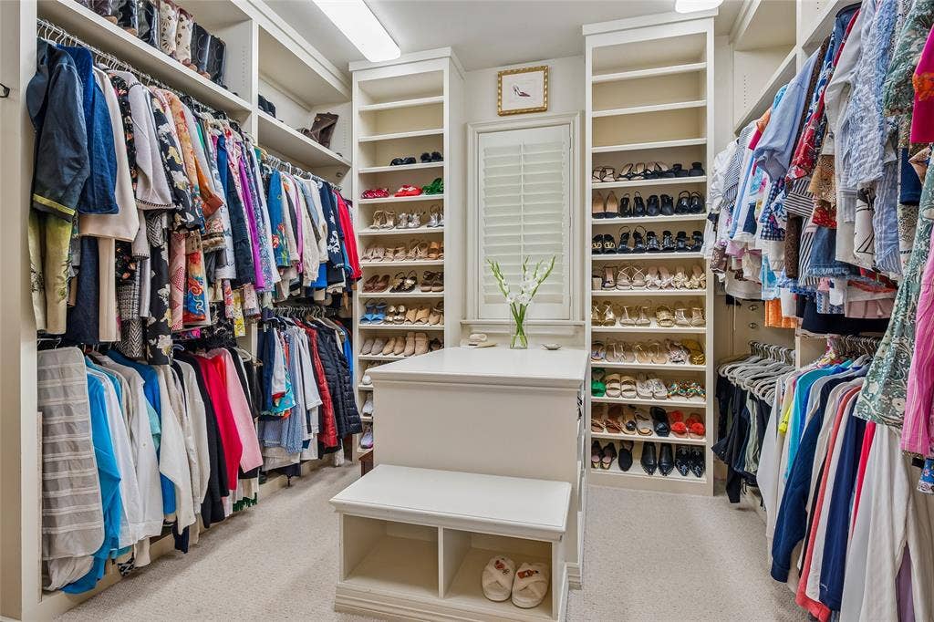 5222 Stonegate Road, Dallas, TX 75209 His-n-Her primary closets with built-in shelving, extensive hanging storage, central island with integrated seating, window with plantation shutters, and recessed lighting fixtures