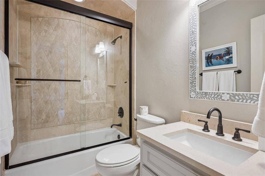 5222 Stonegate Road, Dallas, TX 75209 Bathtub with glass sliding doors, tiled surround with decorative inlay, and matte black fixtures