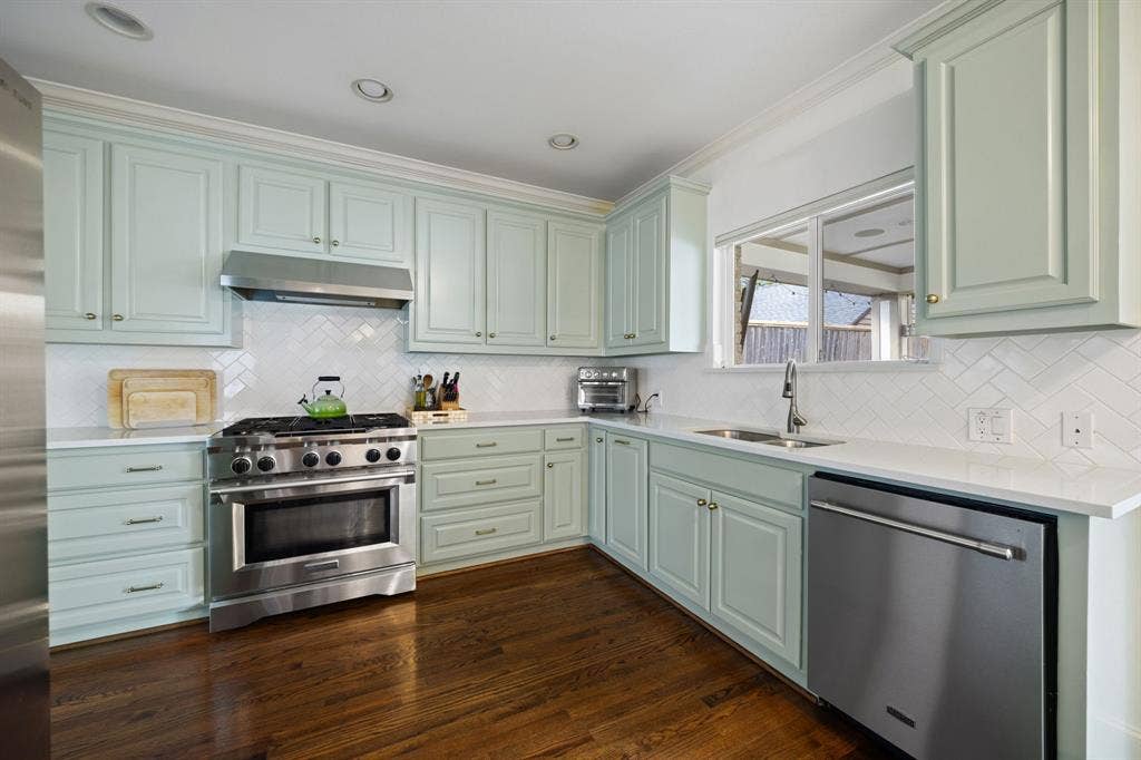 5709 Kenwood Avenue, Dallas, TX 75206 Light-hued cabinetry with ample storage, stainless steel appliances, wood-finish flooring, white countertops, and a herringbone pattern tile backsplash