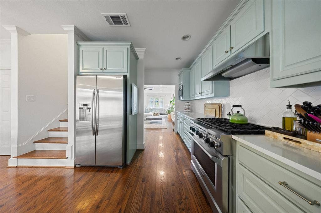 5709 Kenwood Avenue, Dallas, TX 75206 Hardwood flooring throughout, stainless steel refrigerator, stainless steel range, light-toned cabinetry, and white tile backsplash
