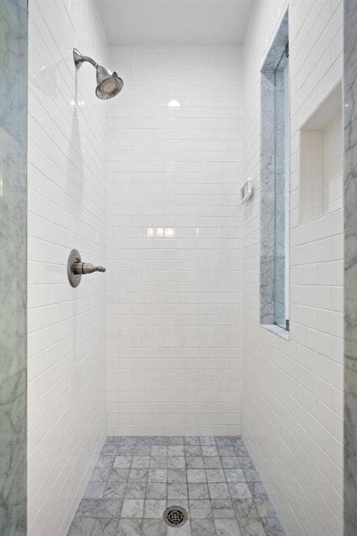 5709 Kenwood Avenue, Dallas, TX 75206 White subway tile shower surround with a built-in niche and window, featuring a brushed nickel shower head and controls, and a grey tile floor with a central drain
