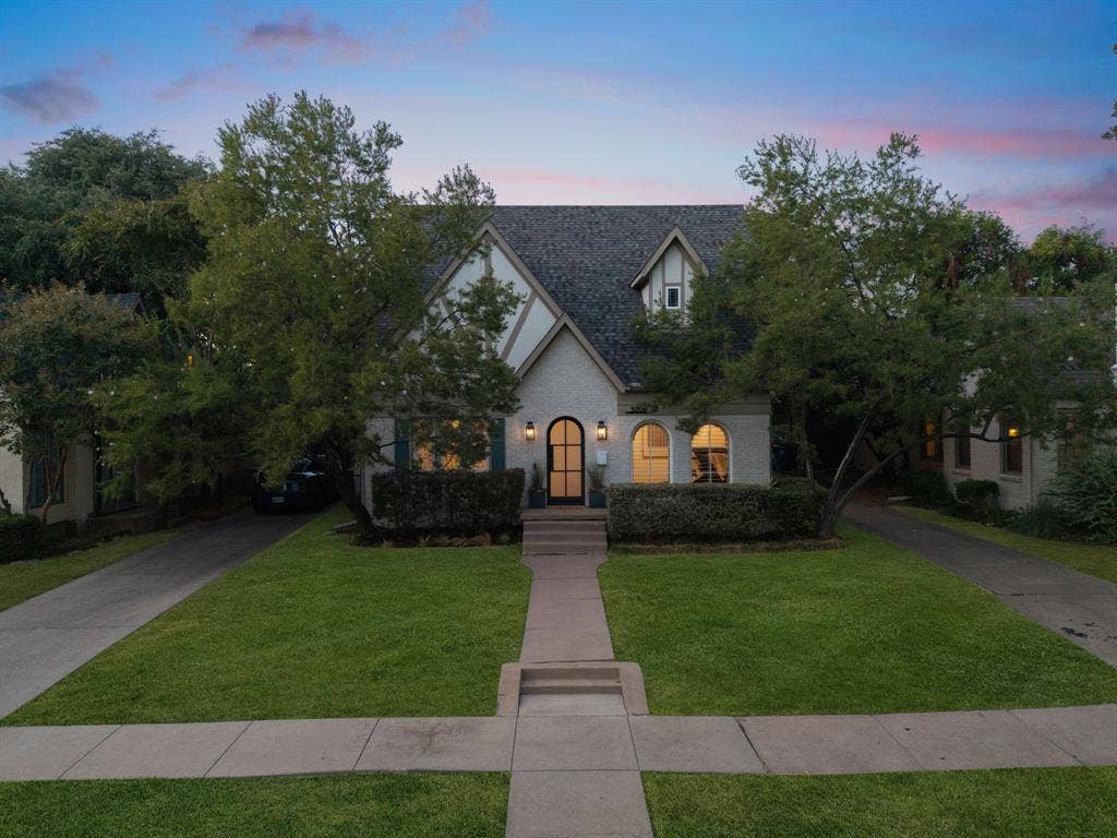 5709 Kenwood Avenue, Dallas, TX 75206 Tudor-style exterior with a dark shingle roof, arched entry door, light brick facade, and dormer windows