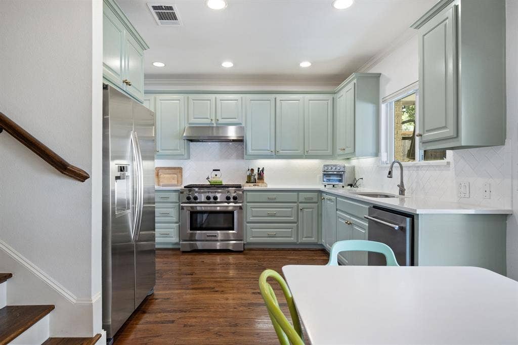 5709 Kenwood Avenue, Dallas, TX 75206 Kitchen featuring light green cabinetry, stainless steel appliances, white countertops, a tiled backsplash, and recessed lighting