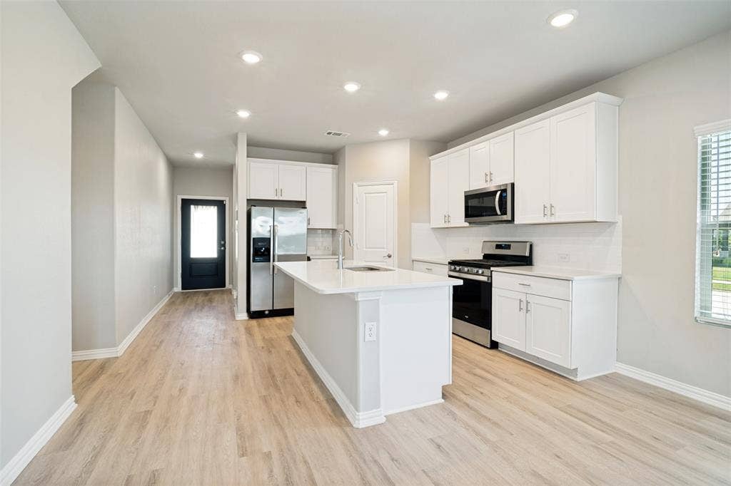 2403 Rocky Mountain Drive, Royse City, TX 75189 Open concept living area with wood-finish flooring, recessed lighting, and a kitchen featuring white cabinetry, a central island, and stainless steel appliances