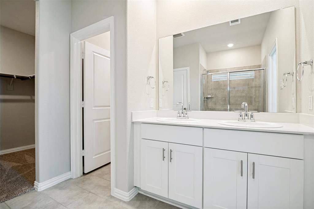 2403 Rocky Mountain Drive, Royse City, TX 75189 Dual vanity with white cabinetry and chrome fixtures, large rectangular mirror, and gray tile flooring