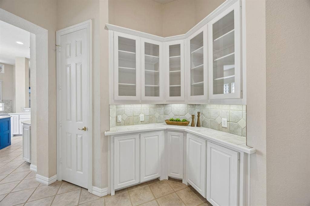 1106 Hills Creek Drive, McKinney, TX 75072 The Butler's pantry offers wonderful space for storing fine china and other treasures in the glass front cabinets as well as storage for service pieces. The counter gives space for staging courses for a dinner or to set out a buffet. The door shown to the left opens to under the stair storage including additional pantry shelving.