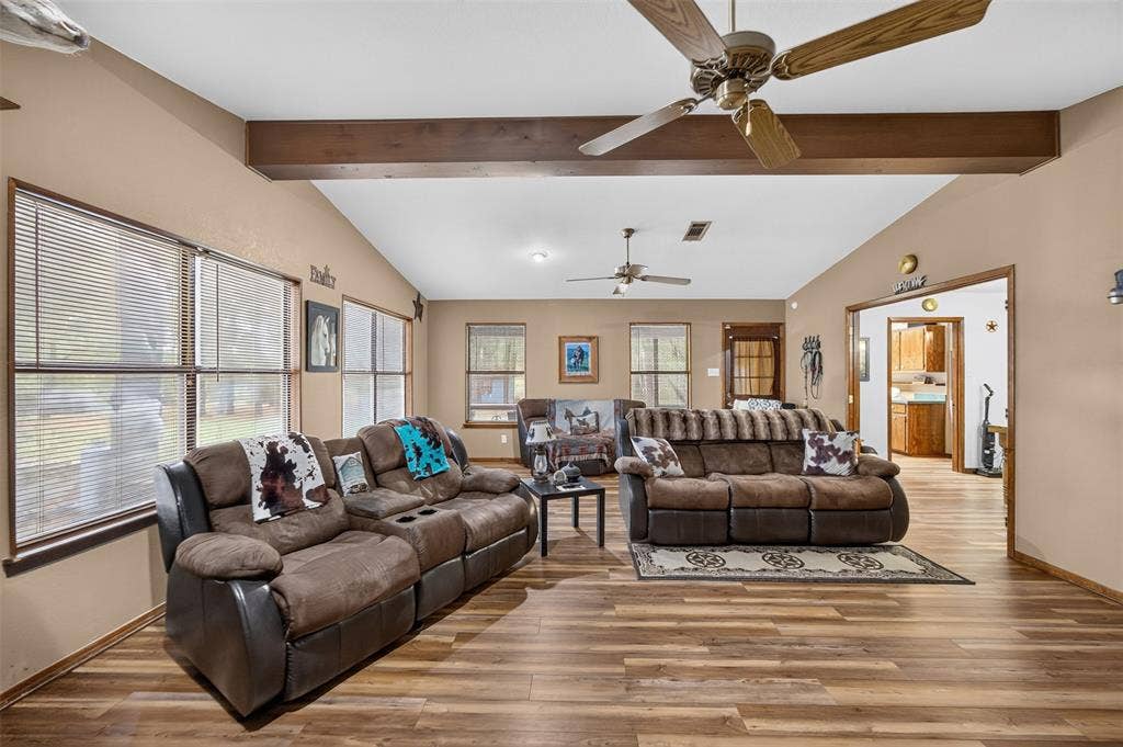 Spacious living area featuring vaulted ceilings with exposed wood beams, wood-finish flooring, and multiple windows