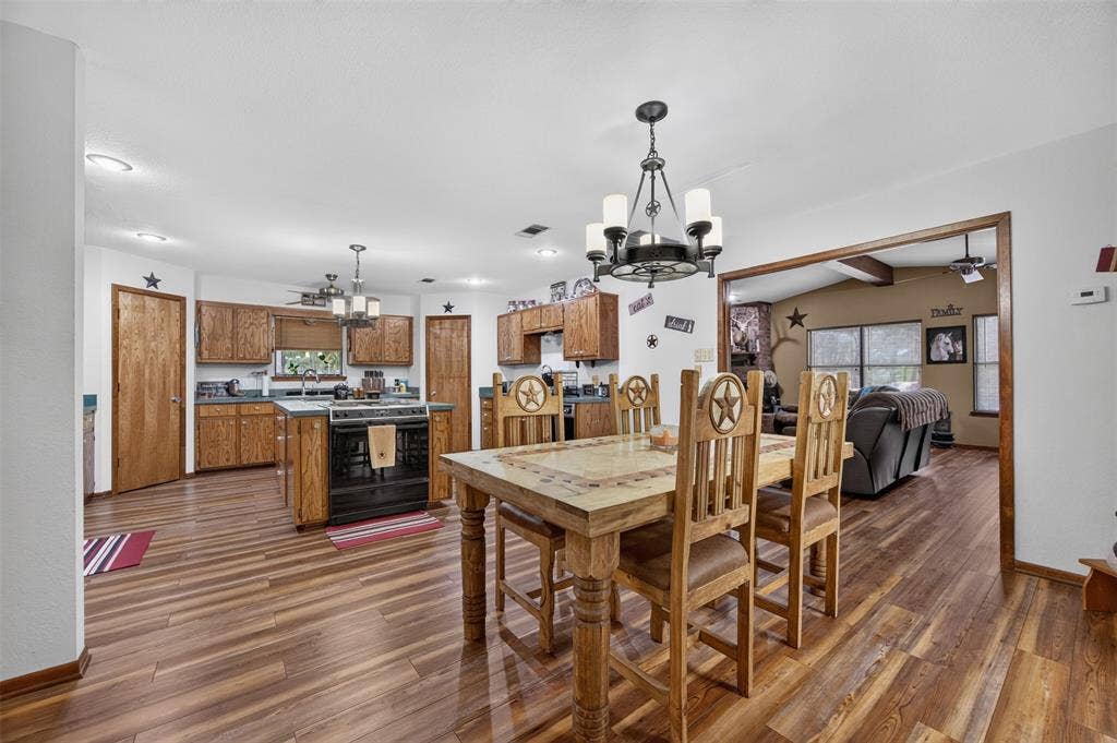 Wood-finish flooring throughout, kitchen with wood cabinetry and dark countertops, kitchen island with built-in range, and recessed lighting