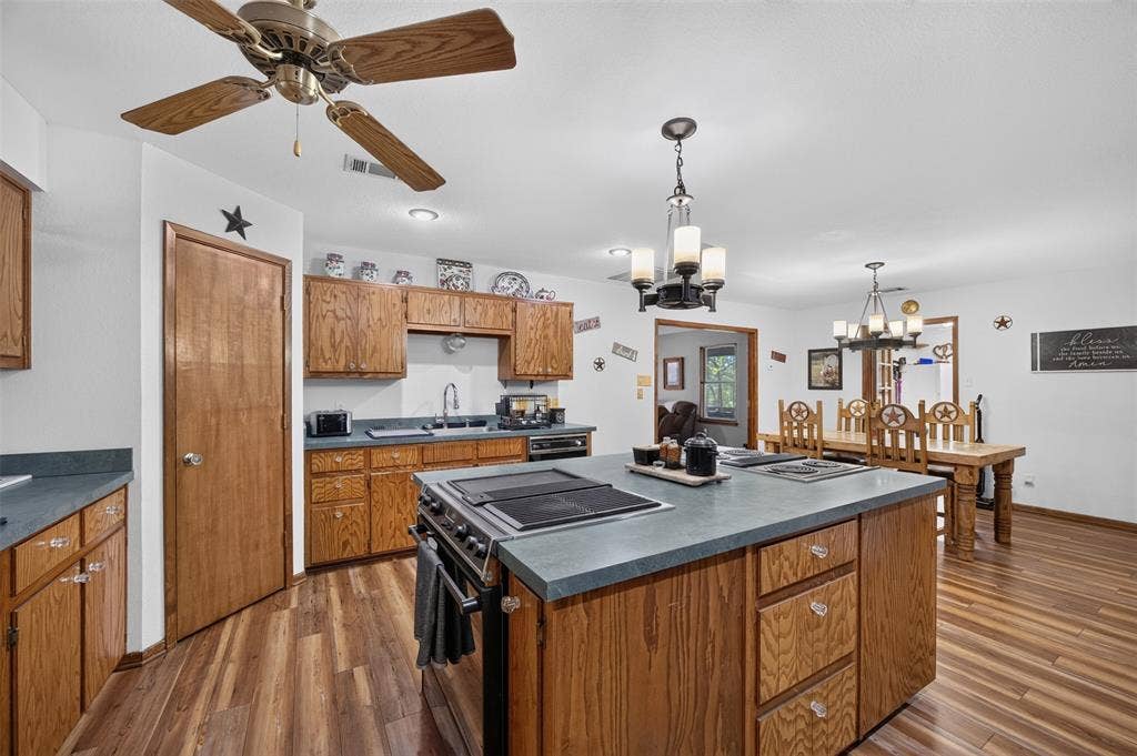 Chef's kitchen featuring wood cabinetry, a large center island with slate countertops and built-in cooktop, stainless steel appliances, and hardwood flooring throughout