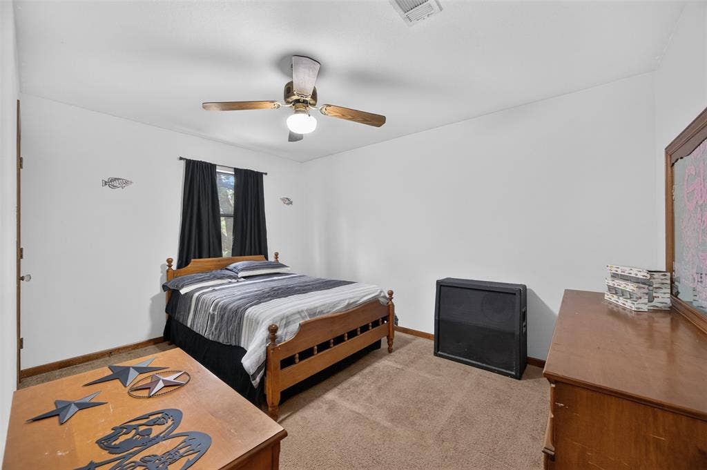 Spacious bedroom featuring hardwood-finish flooring, a wood-frame bed, ceiling fan with integrated lighting, and ample natural light from window with dark curtains