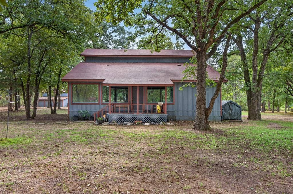 Wooded lot with mature trees, a covered porch, and a utility shed
