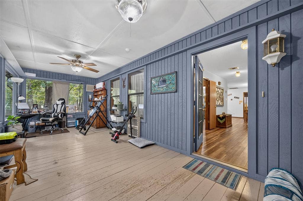 Enclosed porch with wood-finish flooring, blue vertical plank paneling, and multiple windows