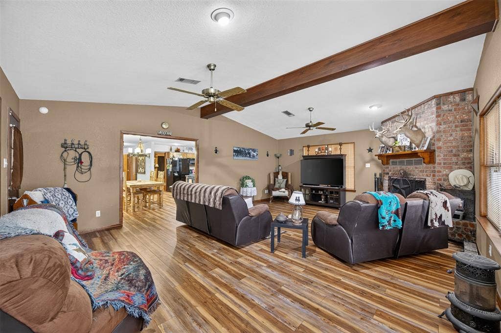 Vaulted ceiling, exposed wood beams, wood-finish flooring, brick-faced fireplace, and an open doorway