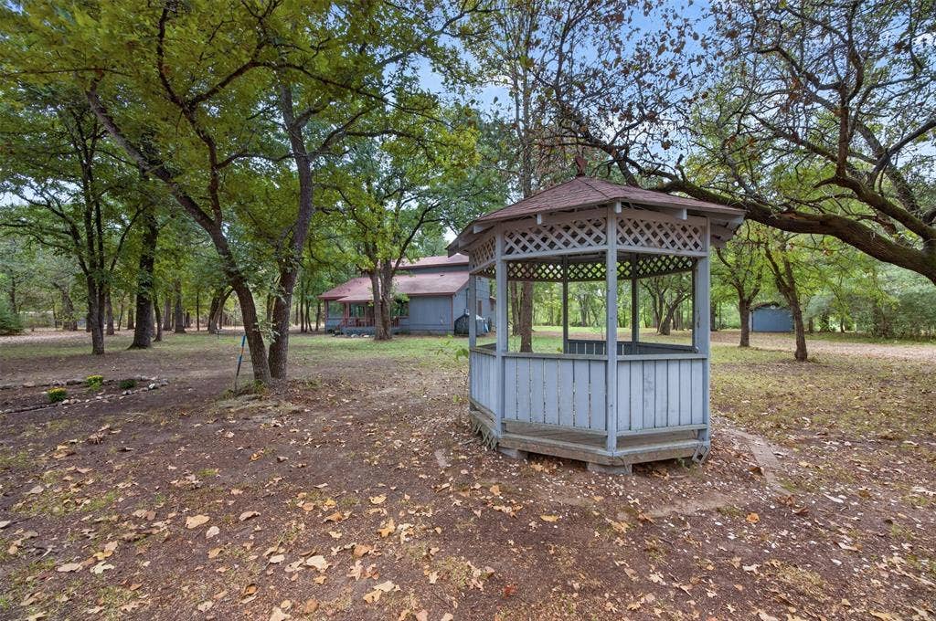 Wooden gazebo with lattice detailing and a shingled roof, surrounded by mature trees