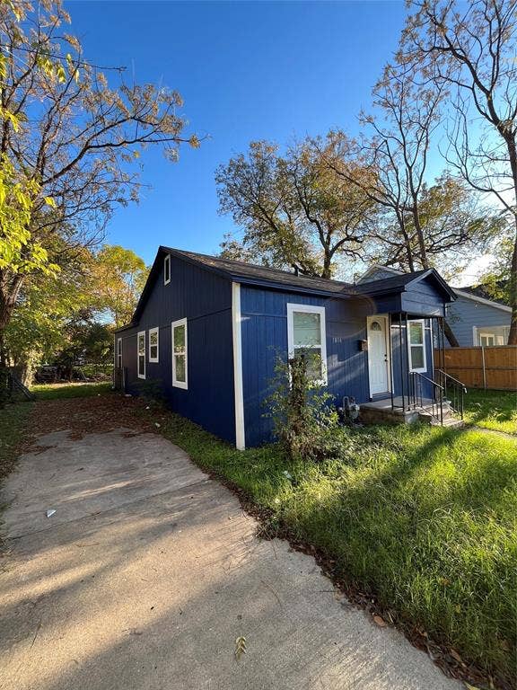 3806 Pine Street, Dallas, TX 75210 Exterior featuring blue vertical siding, a front porch with metal railing, concrete driveway, and mature trees