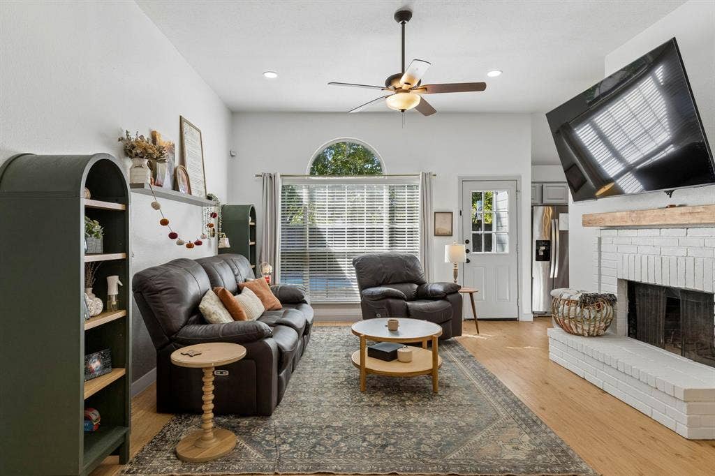 1111 Hyde Park Drive, McKinney, TX 75069 The spacious living room features a painted white brick wood burning fireplace, ceiling fan, LVP flooring, recessed lighting and views of the backyard.