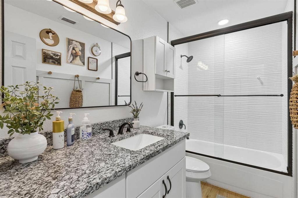 1111 Hyde Park Drive, McKinney, TX 75069 The secondary bathroom displays a large tub in shower with wavy tile, granite counter tops, a framed mirror LVP flooring, recessed lighting, and ample counter and cabinet space.
