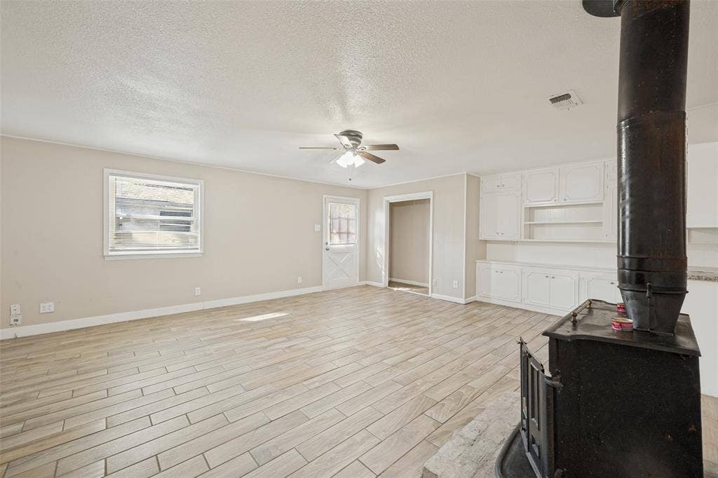 213 W Dorris Drive, Grand Prairie, TX 75051 Spacious living area featuring wood-finish tile flooring, a built-in wood-burning stove, white built-in cabinetry, and a ceiling fan