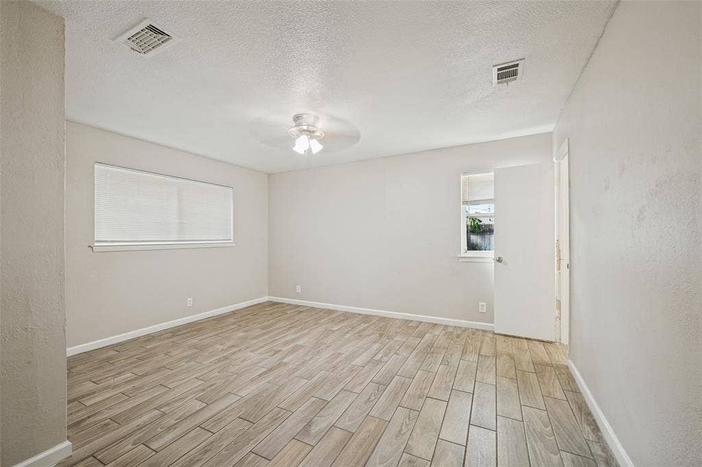 213 W Dorris Drive, Grand Prairie, TX 75051 Spacious room featuring wood-finish tile flooring, neutral wall tones, window blinds, and a ceiling fan with integrated lighting